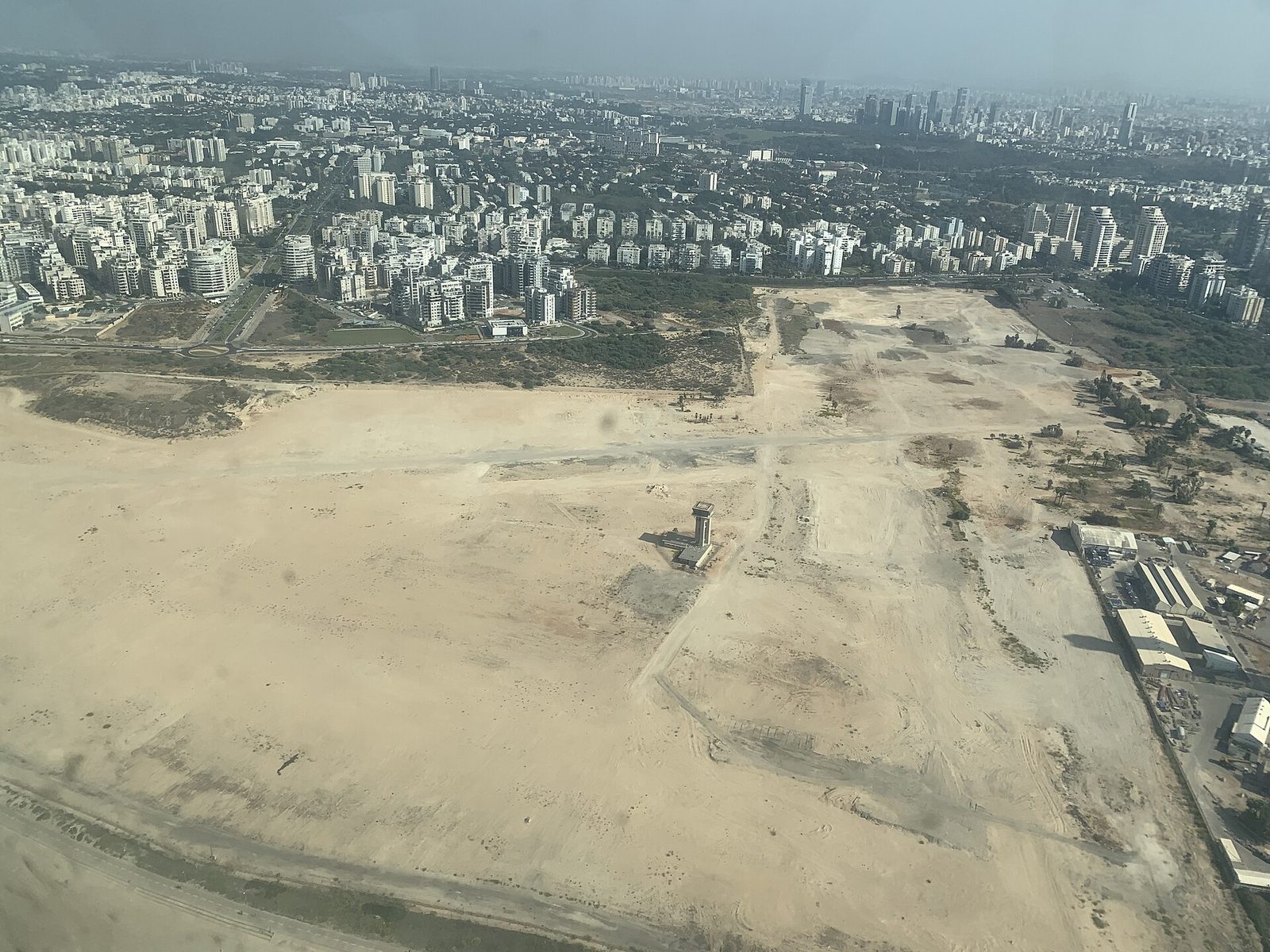 שטח שדה דב לשעבר, לפני הבנייה, עם מגדל הפיקוח הישן ותל אביב ברקע